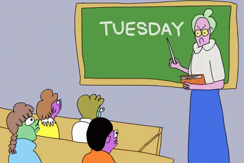 Teacher Standing in Front of Tuesday Blackboard