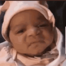 The Baby Is Wearing A Pink Hat And Making A Sad Face . GIF