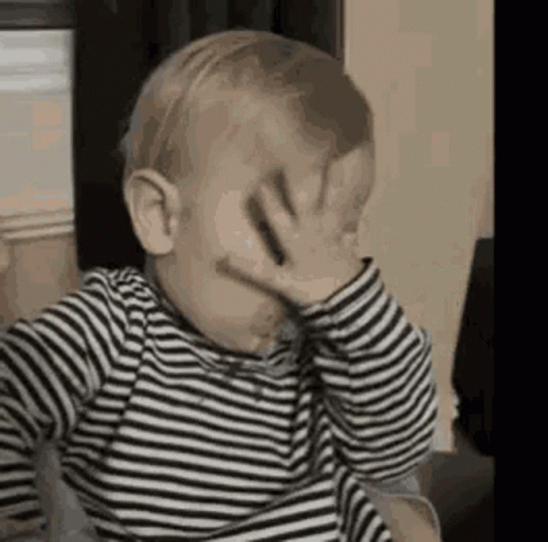The Baby Is Wearing A Striped Shirt And Covering His Face With His Hand . GIF