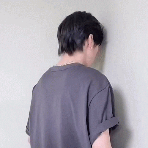 The Back Of A Person Wearing A Gray T-Shirt Is Leaning Against A Wall . GIF