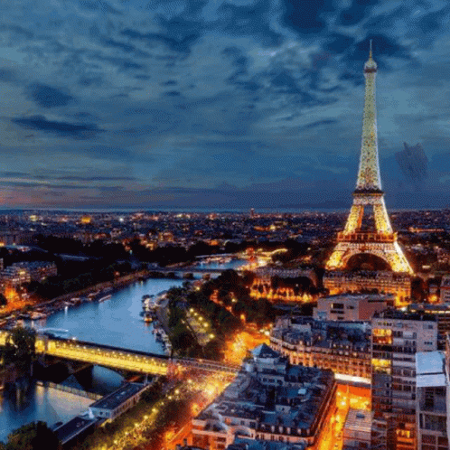 The Eiffel Tower Is Lit Up At Night With A Blue Sky In The Background GIF