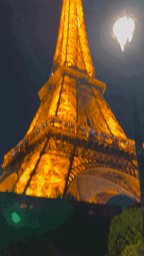 The Eiffel Tower Is Lit Up At Night With A Full Moon GIF