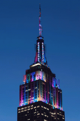 The Empire State Building Is Lit Up With Colorful Lights At Night GIF