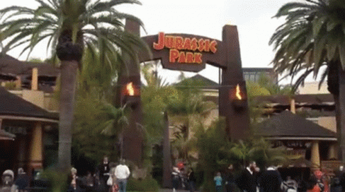 The Entrance To Jurassic Park Is Shown With Palm Trees In The Background GIF
