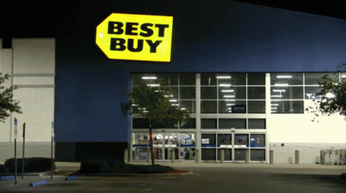 The Front Of A Best Buy Store At Night With A Parking Lot In Front Of It GIF