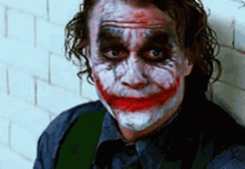 The Joker Is Leaning Against A Wall With His Face Painted And Making A Funny Face . GIF