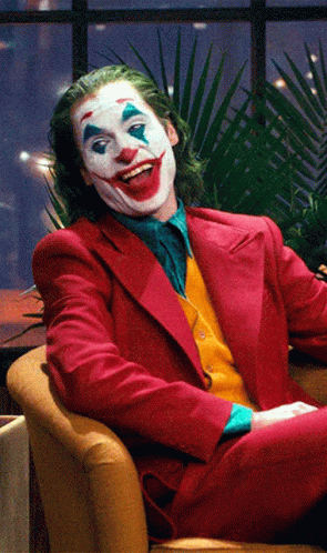 The Joker Is Sitting In A Chair And Smiling GIF