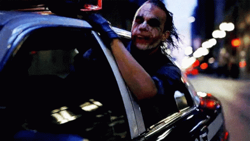 The Joker Is Sitting In The Back Of A Police Car And Looking Out The Window . GIF