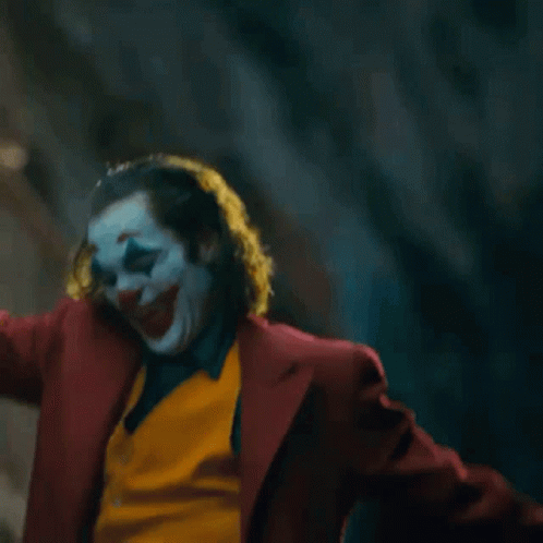 The Joker Is Standing On A Set Of Stairs With His Arms Outstretched . GIF