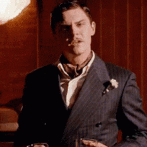 The Man Is Wearing A Suit And Tie And Holding A Glass Of Whiskey . GIF