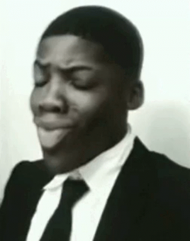 The Man Is Wearing A Suit And Tie And Making A Funny Face . GIF