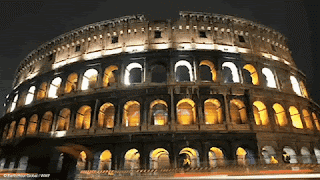 The Roman Colosseum Is Lit Up At Night And Has Arches And Windows GIF