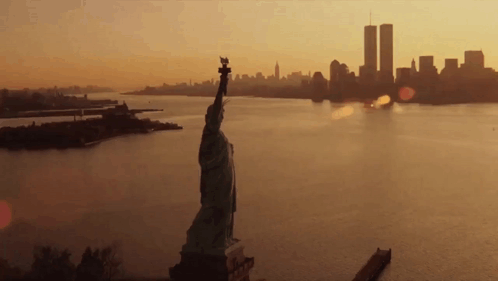 The Statue Of Liberty Is In The Foreground And The Twin Towers In The Background GIF