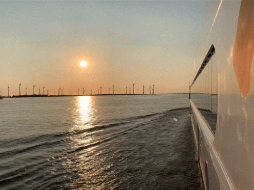 The Sun Is Setting Over A Body Of Water With Wind Turbines In The Background GIF