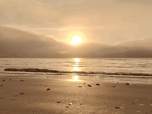 The Sun Is Setting Over The Ocean And Mountains In The Background GIF