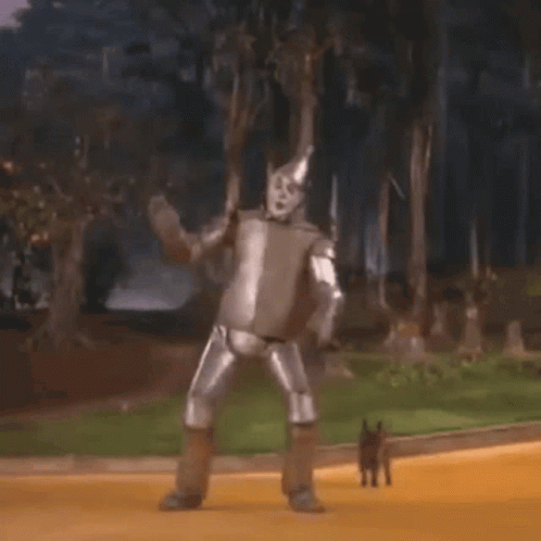 The Tin Man From The Wizard Of Oz Is Dancing On The Yellow Brick Road With A Dog . GIF