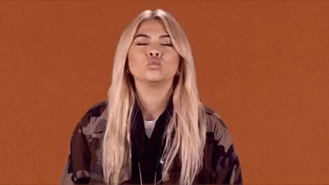 The Woman Is Wearing A Camouflage Jacket And Blowing A Kiss . GIF