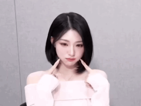 The Woman Is Wearing A White Off The Shoulder Top And Making A Heart Shape With Her Hands . GIF