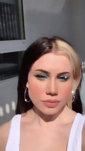 The Woman Is Wearing A White Tank Top And Earrings . GIF