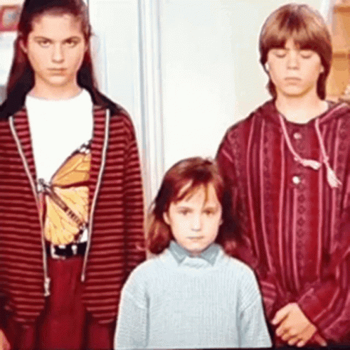 Three Children Are Standing Next To Each Other In A Room . One Of The Children Is Wearing A Butterfly Shirt . GIF