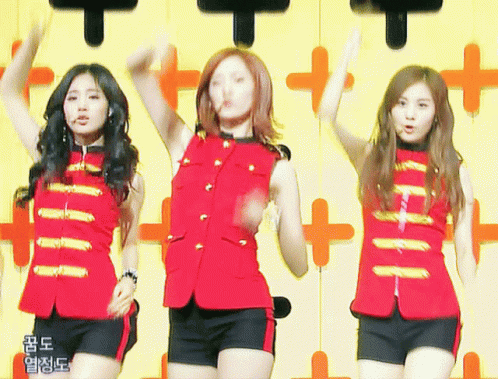 Three Girls Are Dancing In Front Of A Yellow Wall With Chinese Writing GIF