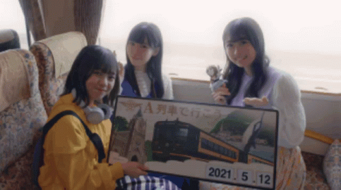 Three Girls Sitting On A Bus Holding A Sign That Says 2021.05.12 GIF