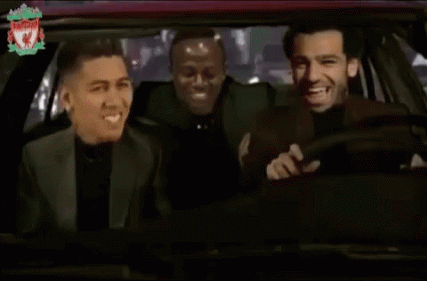 three men are laughing in a car with the liverpool logo on the bottom right