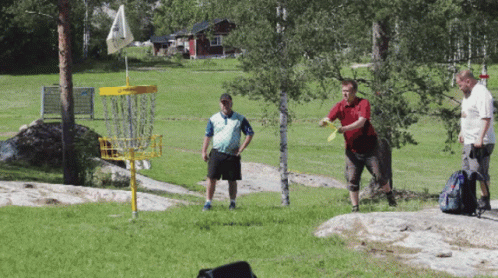 three men are playing frisbee golf in a field with a yellow frisbee basket