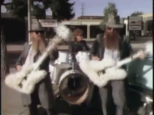 Three Men Are Playing Guitars And Drums In A Band On A Sidewalk . GIF