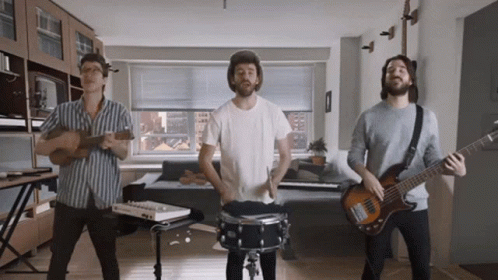 Three Men Are Playing Instruments In A Living Room And One Is Playing A Bass Guitar GIF