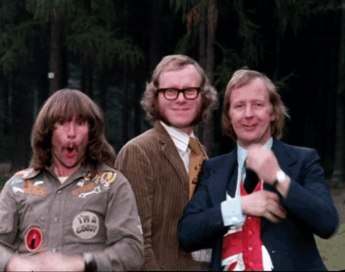 Three Men Are Posing For A Picture And One Of Them Has A Patch On His Shirt That Says Twa Goody GIF