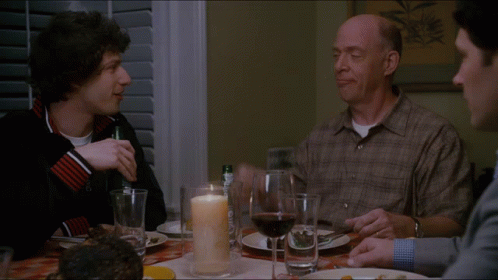 Three Men Are Sitting At A Table With A Candle And Wine GIF