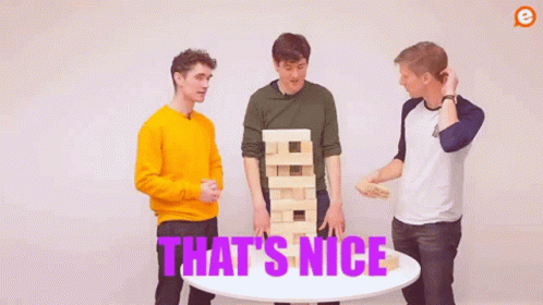 Three Men Are Standing Around A Table With A Jenga Tower . GIF