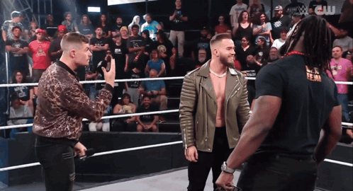 three men are standing in a wrestling ring and one of them is wearing a black t-shirt that says w.c.