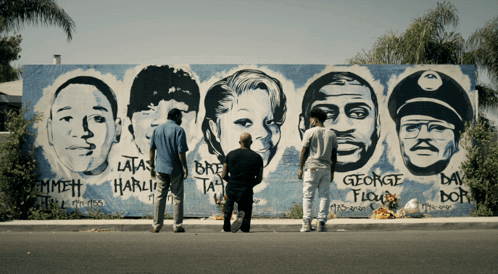 Three Men Are Standing In Front Of A Mural Of George Floyd 'S Face GIF