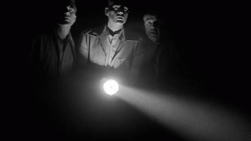 Three Men Are Standing In The Dark Holding A Light . GIF