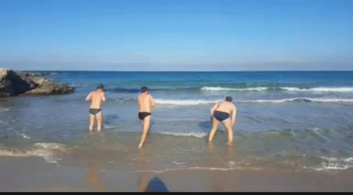 Three Men Are Standing In The Water On A Beach GIF