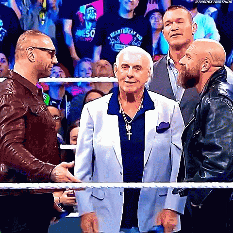Three Men Are Standing Next To Each Other In A Wrestling Ring Talking To Each Other . GIF
