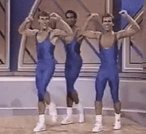 Three Men In Blue Jumpsuits Are Flexing Their Muscles On A Stage GIF