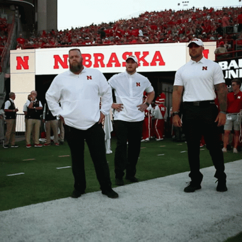 Three Men on Football Field in Front of Nebraska Sign
