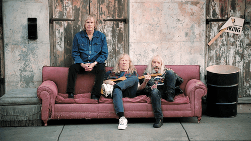 Three Men on Pink Couch in Front of Building With No Parking Sign