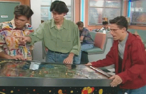 Three Men Playing Pinball Machine in Diner With TNT Sign
