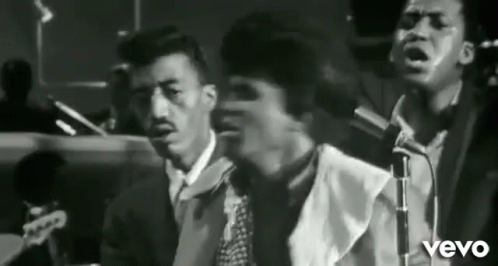 Three Men Singing into Microphones in Band