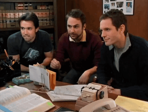 Three Men Sitting at Desk With Papers and Phone