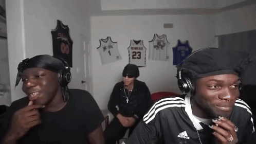 three men wearing headphones are sitting in a room with jerseys hanging on the wall including one with the number 23 on