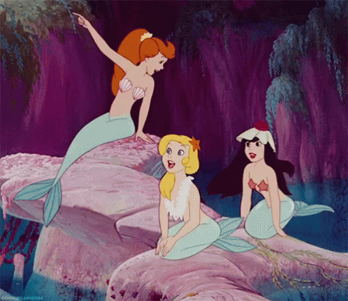 Three Mermaids Are Sitting On A Rock And One Of Them Is Pointing GIF