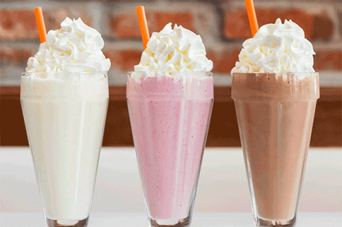 Three Milkshakes With Whipped Cream And Straws On Top GIF