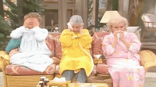 Three Older Women Are Sitting On A Couch Blowing Their Noses With Tissues . GIF
