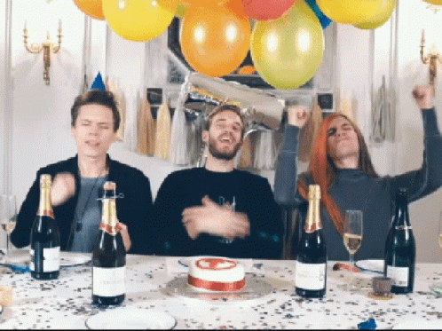Three People Are Sitting At A Table With Bottles Of Champagne And A Birthday Cake GIF