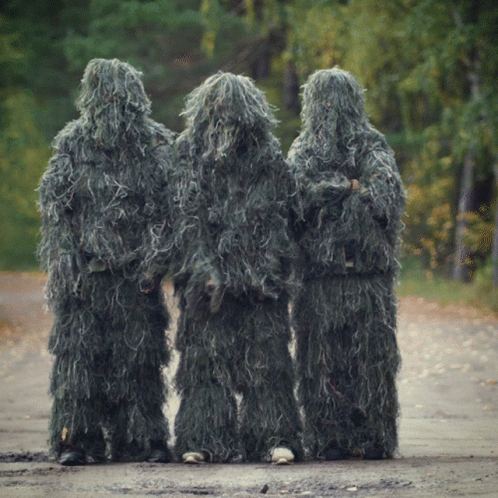 Three People Are Standing On A Dirt Road Wearing Sniper Suits GIF